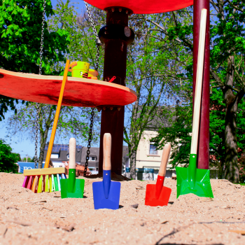 Ein Sandkasten mit unserem Sandkasten-Set bestehend aus der Sandschaufel, links zu sehen, der kinderschaufel, mittig platziert und dem Kinderbesen Kunterbunt auf der rechten Seite